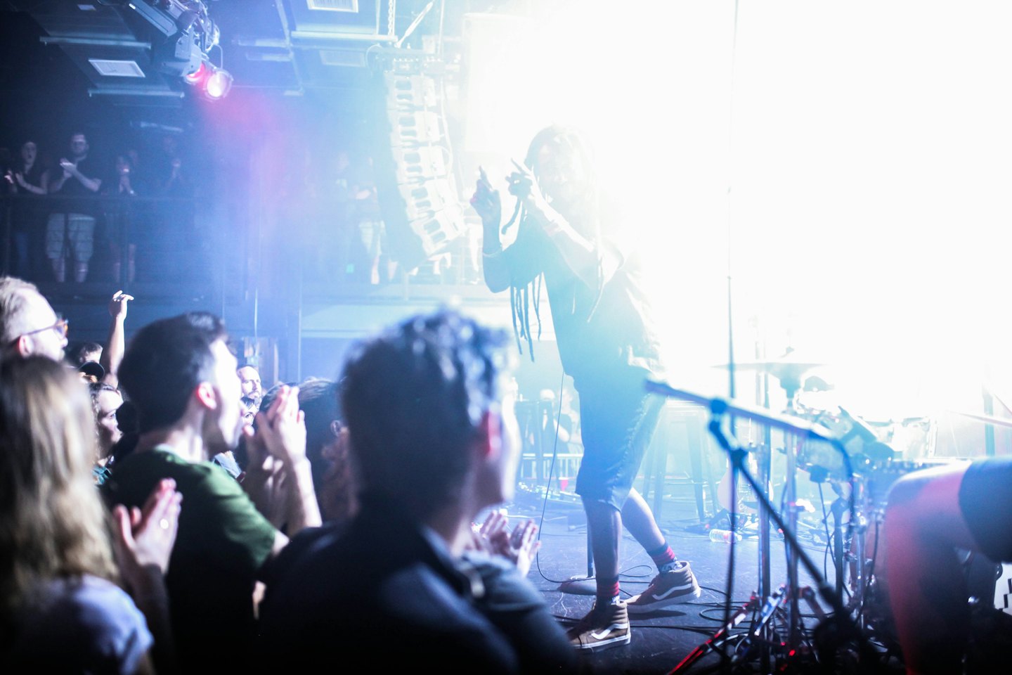 Male performer with dreadlocks on concert stage singing to cheering audience.